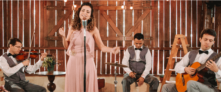 Uma mulher cantando, um homem tocando violão, outro tocando violino e outro tocando cajon.