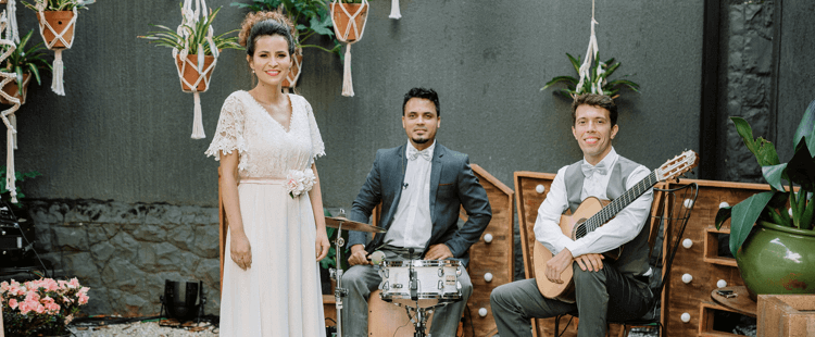 Uma mulher cantando, um homem tocando violão e outro tocando cajon.